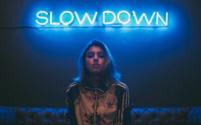 girl sitting on a couch with a neon board that reads "Slowdown"