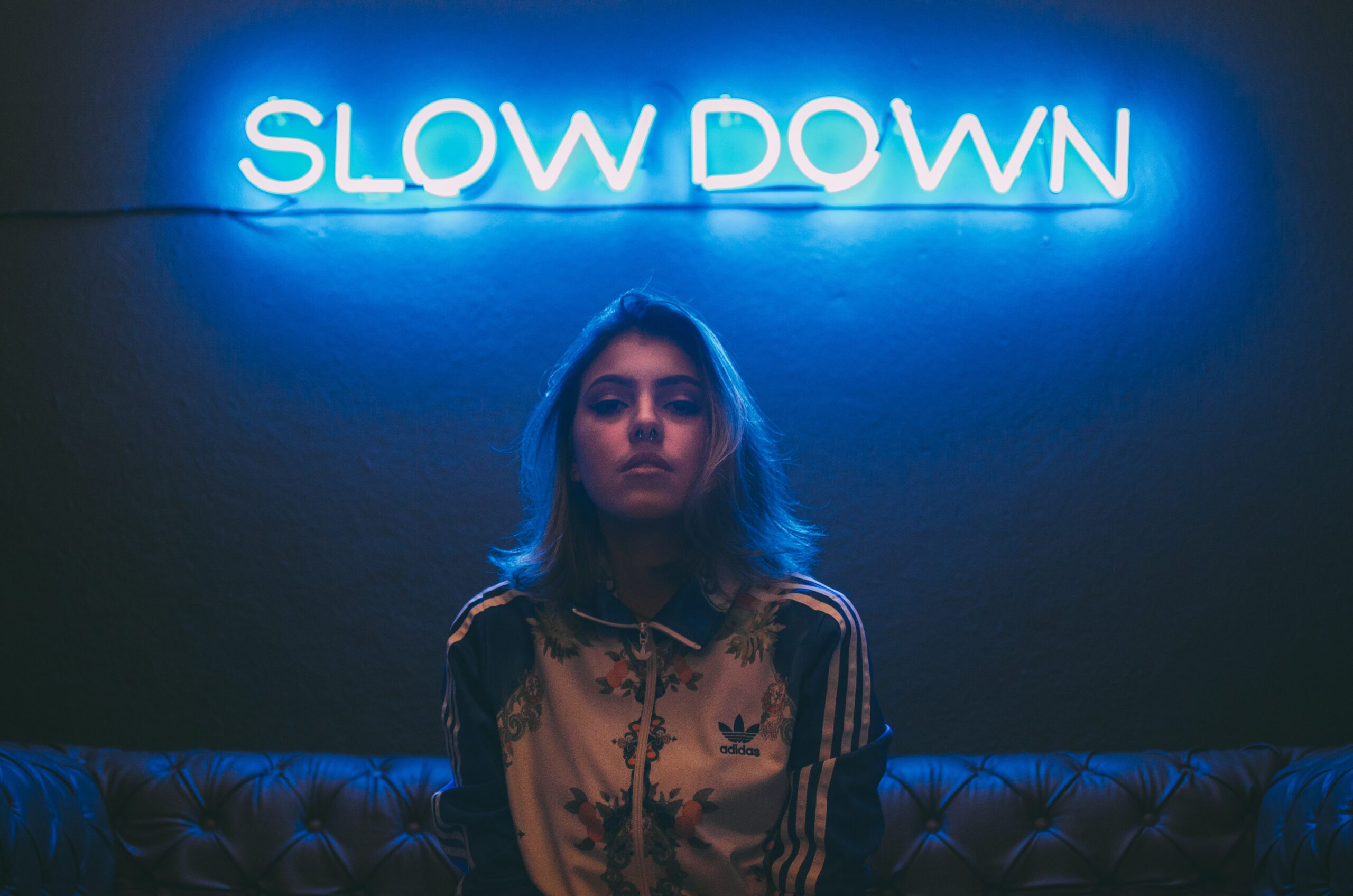 girl sitting on a couch with a neon board that reads "Slowdown"